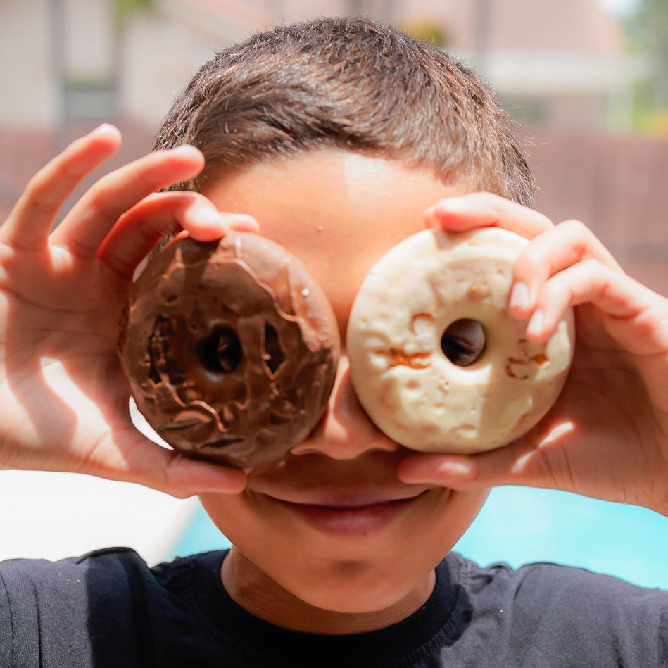 Child holding two donuts over their eyes with a blurred background